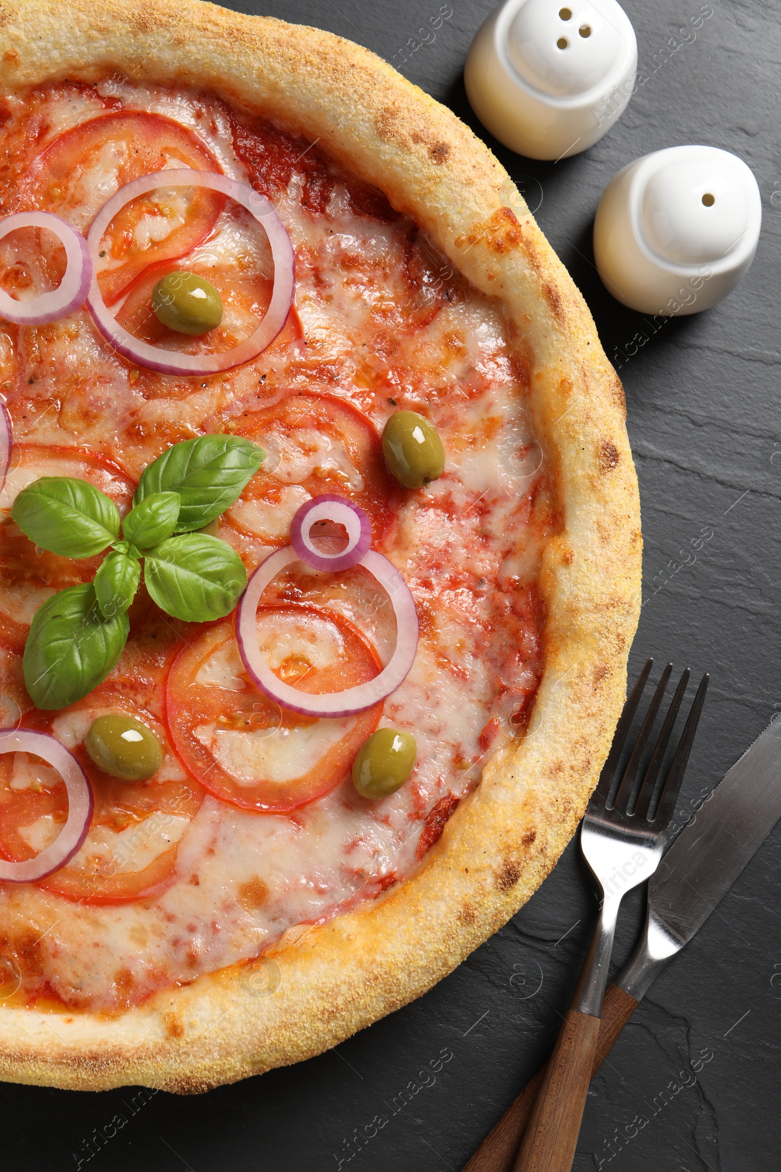 Photo of Delicious vegetarian pizza, cutlery, salt and pepper on black table, top view