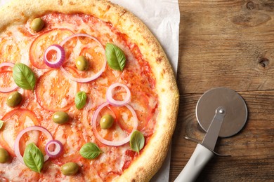 Delicious vegetarian pizza and cutter on wooden table, top view