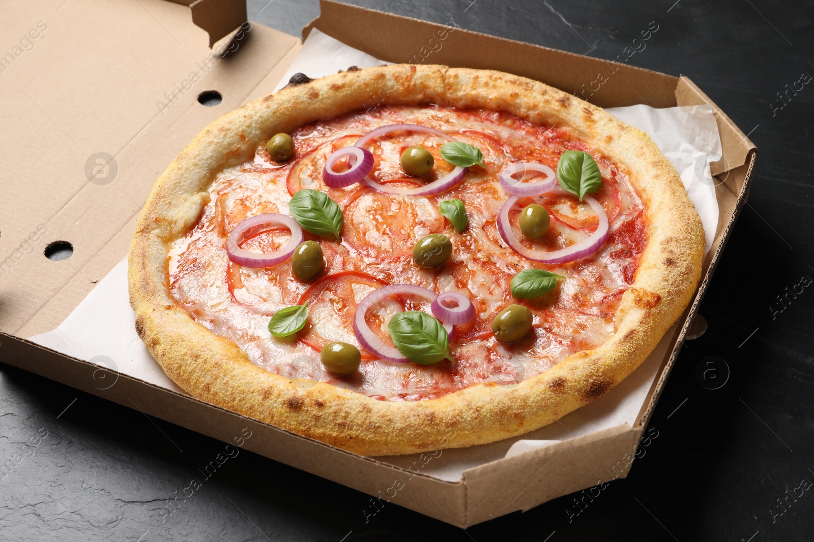 Photo of Delicious vegetarian pizza in box on black table, closeup