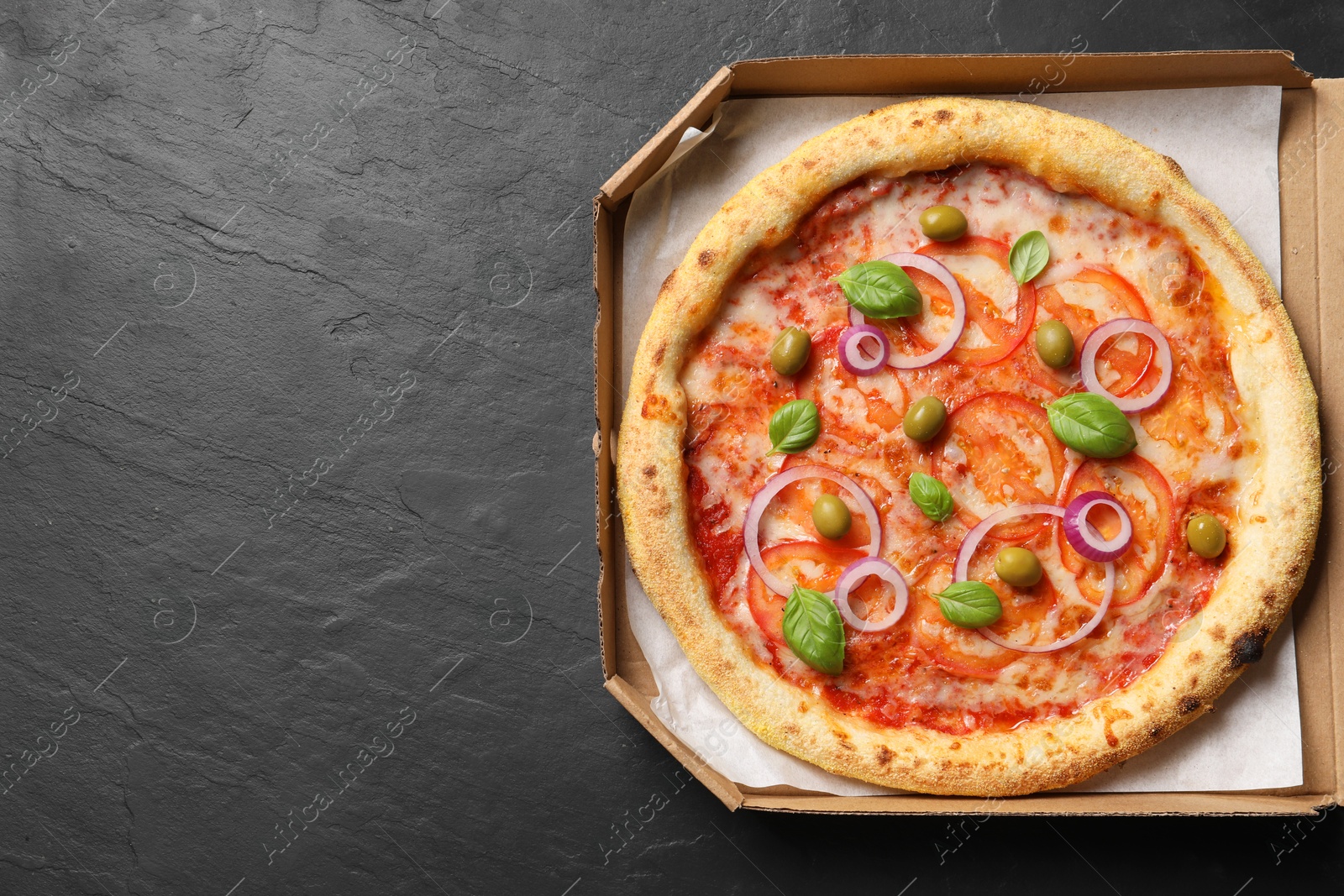 Photo of Delicious vegetarian pizza in box on black table, top view. Space for text