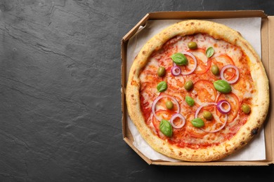 Photo of Delicious vegetarian pizza in box on black table, top view. Space for text