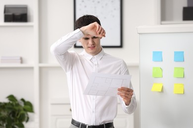 Photo of Embarrassed man with document near white board in office