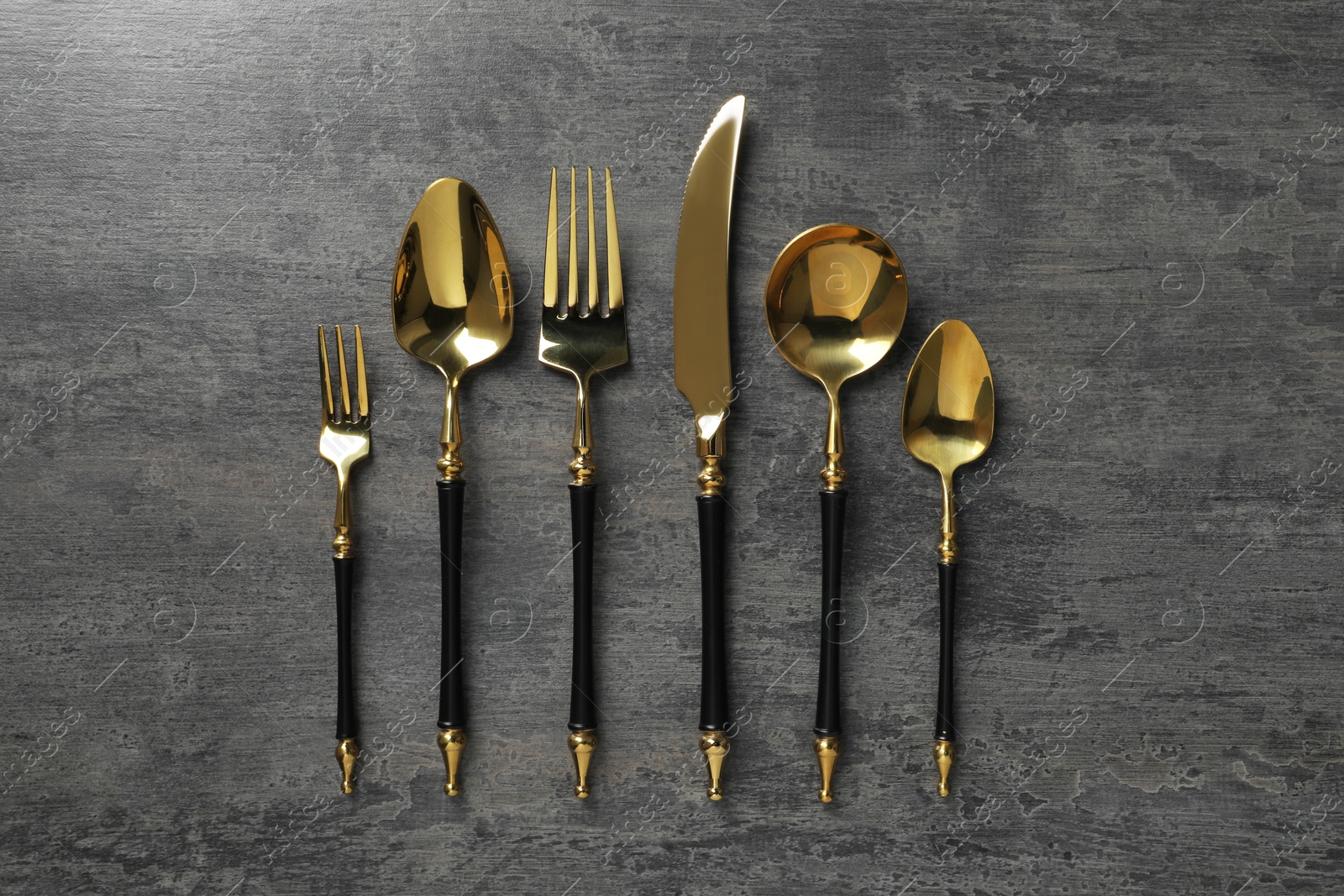 Photo of Elegant golden cutlery set on dark grey table, flat lay