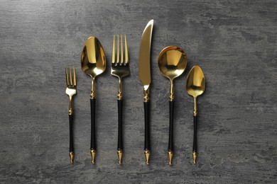 Photo of Elegant golden cutlery set on dark grey table, flat lay