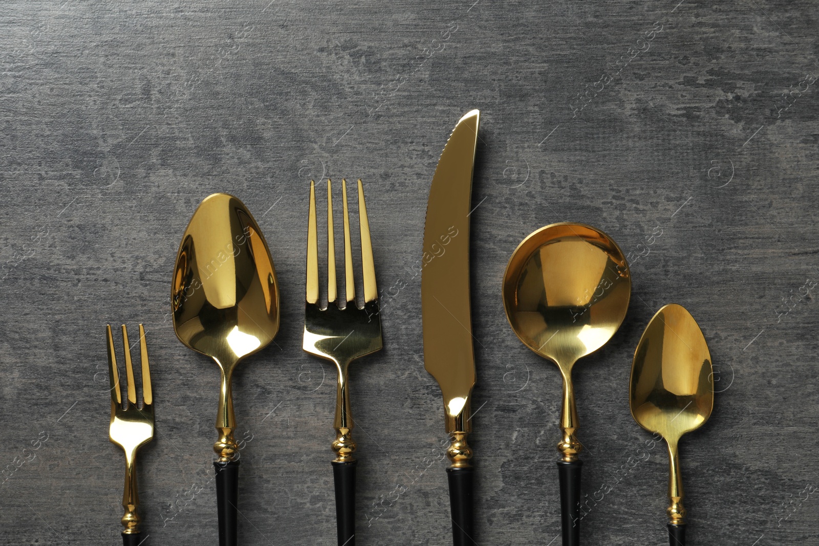 Photo of Elegant golden cutlery set on dark grey table, flat lay