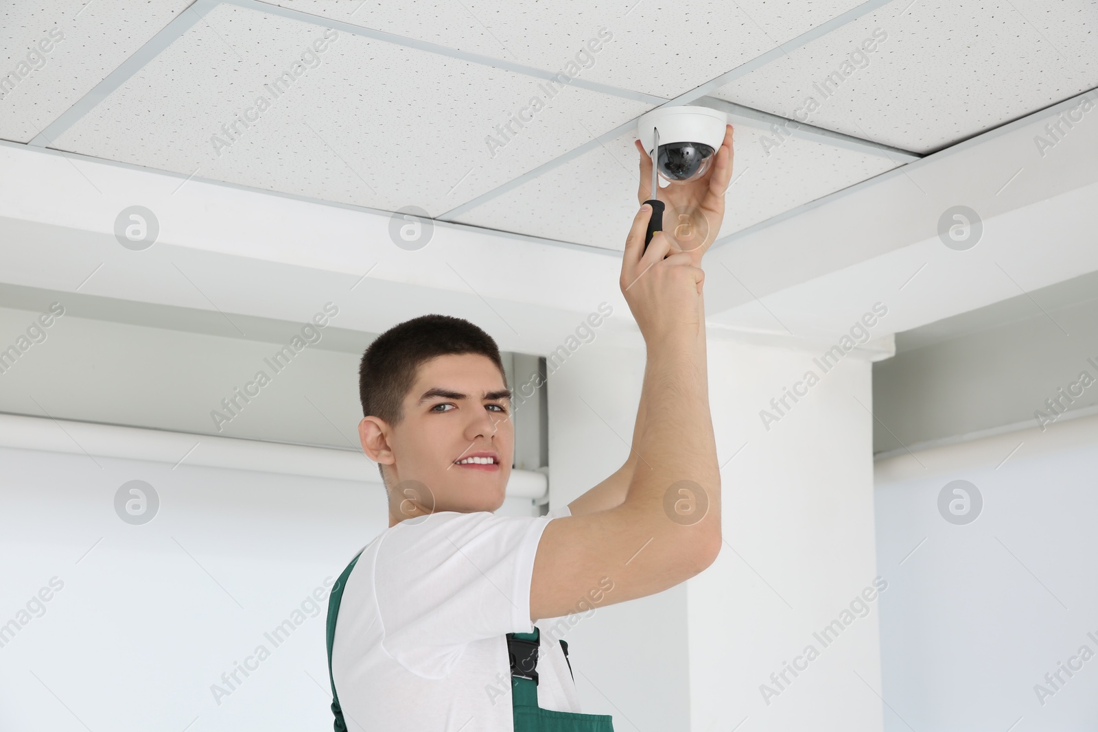 Photo of Technician with screwdriver installing CCTV camera on ceiling indoors