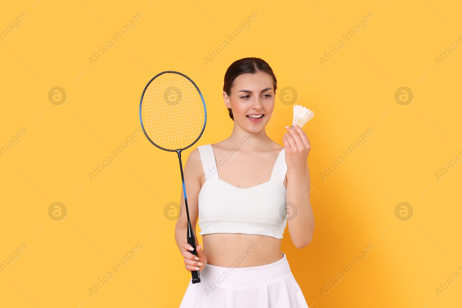 Photo of Young woman with badminton racket and shuttlecock on orange background