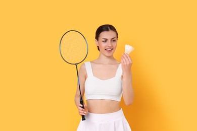 Young woman with badminton racket and shuttlecock on orange background