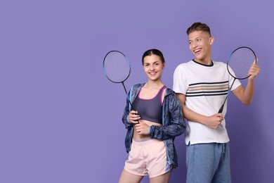 Young man and woman with badminton rackets on purple background, space for text