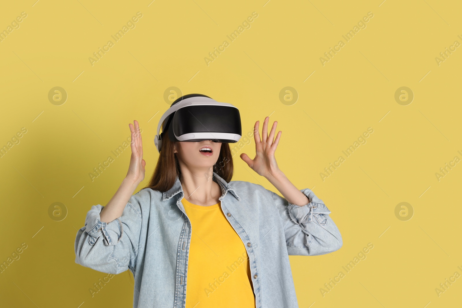 Photo of Surprised woman using virtual reality headset on yellow background