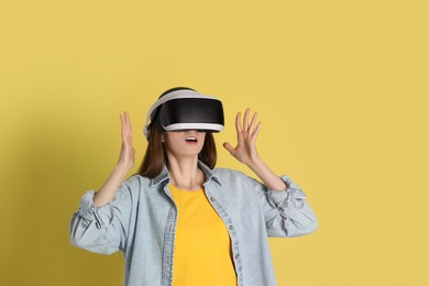 Surprised woman using virtual reality headset on yellow background