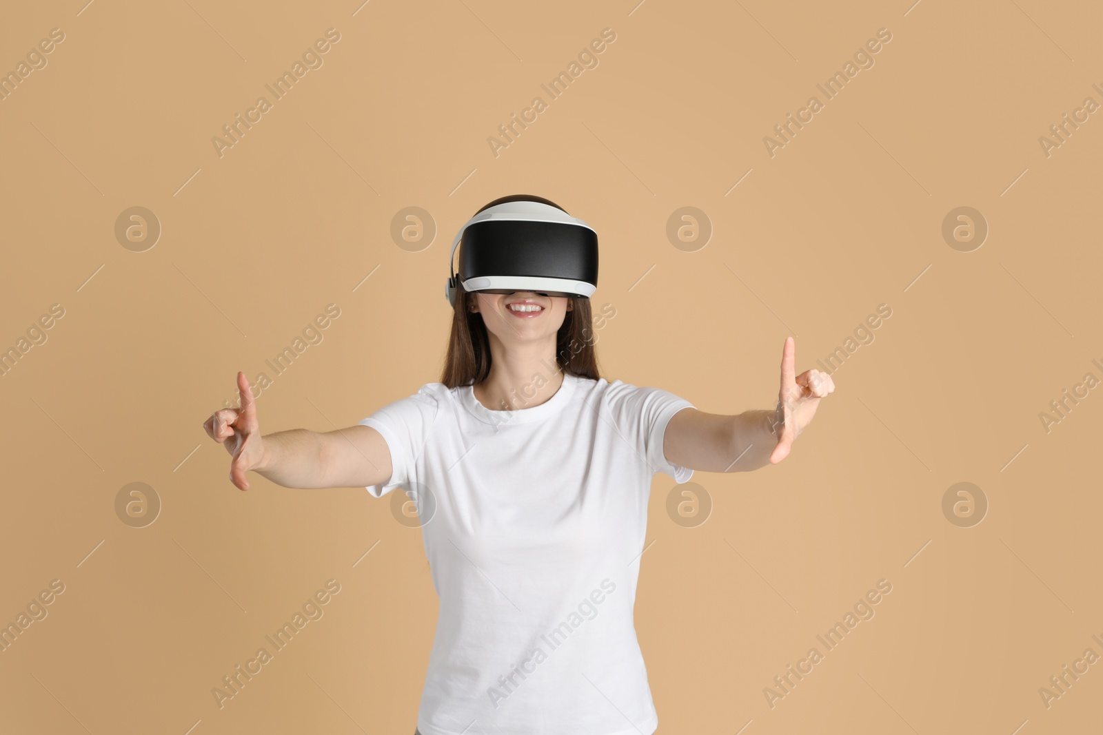 Photo of Smiling woman using virtual reality headset on beige background