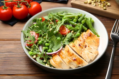 Photo of Healthy meal. Tasty salad and chicken breast in bowl on wooden table