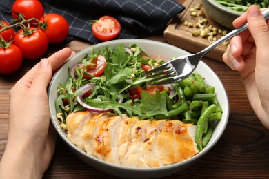 Healthy meal. Woman with bowl of tasty products at wooden table, closeup