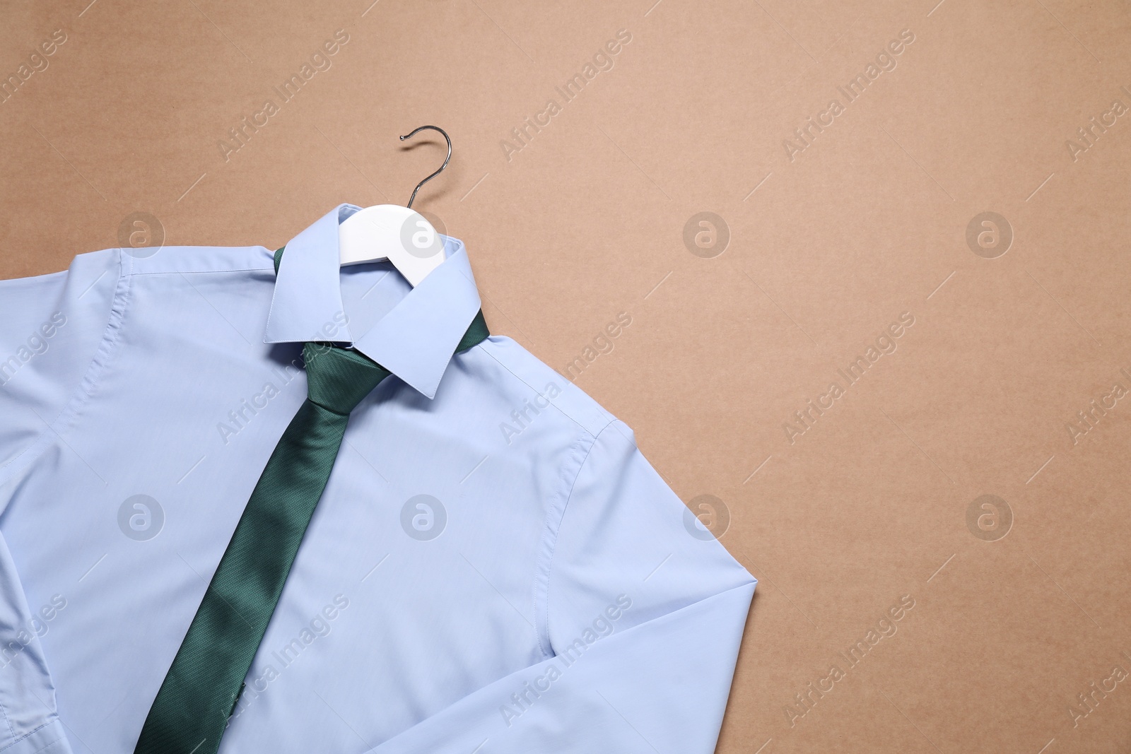 Photo of Hanger with shirt and necktie on beige background, top view. Space for text