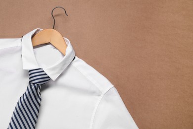 Photo of Hanger with shirt and striped necktie on beige background, top view. Space for text