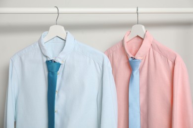 Hangers with shirts and neckties on light background