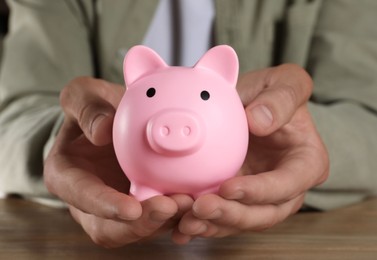 Photo of Man with pink piggy bank on wooden table, closeup