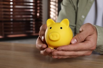 Man with yellow piggy bank on wooden table, closeup