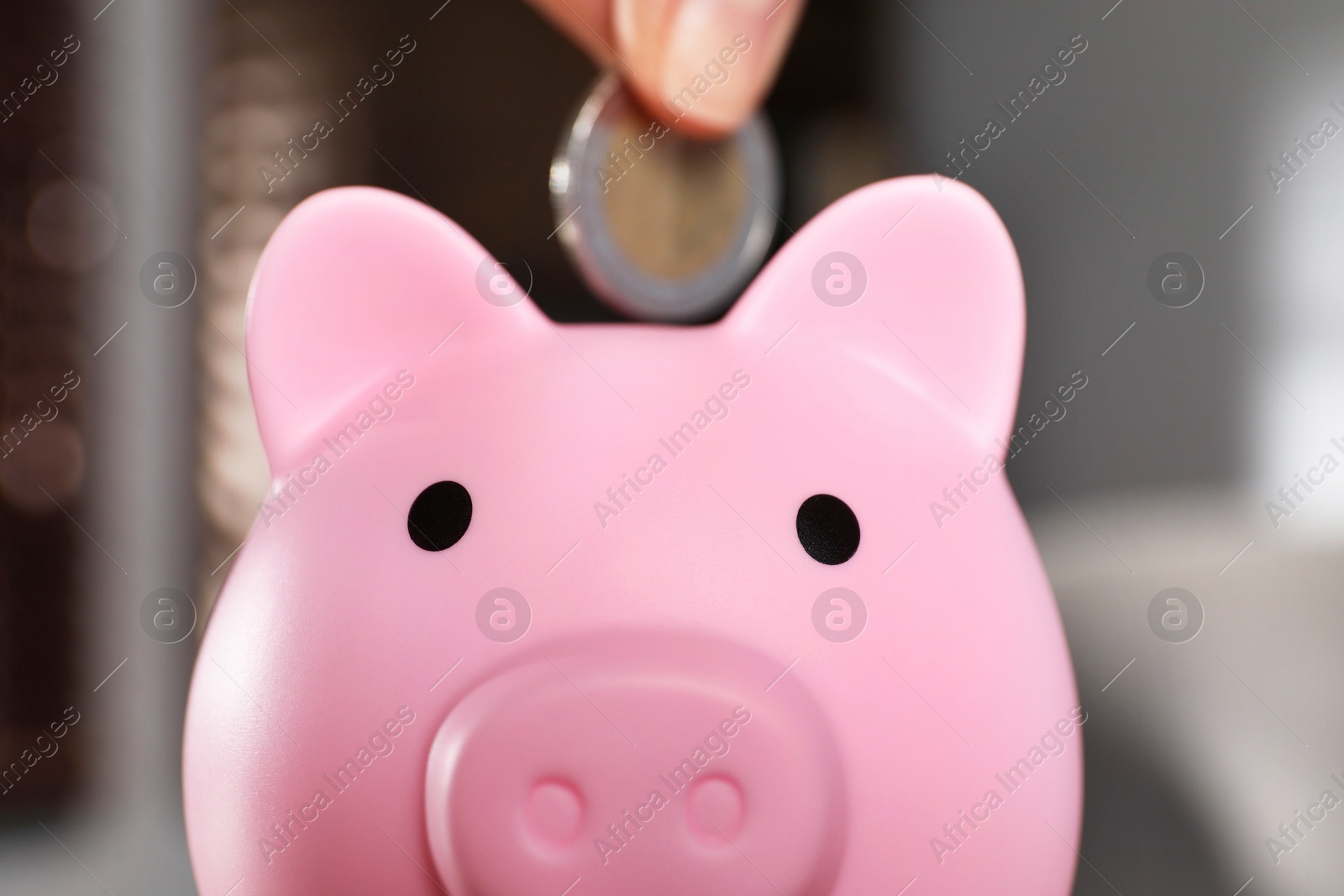 Photo of Woman putting coin into pink piggy bank on blurred background, closeup