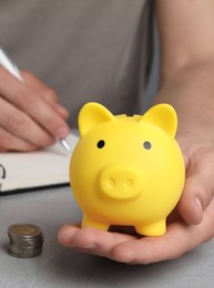 Photo of Man with yellow piggy bank, coins and notebook at grey table, closeup