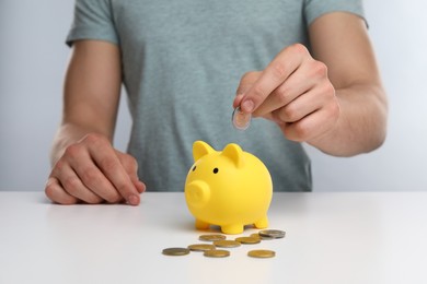 Man putting coin into yellow piggy bank at white table, closeup