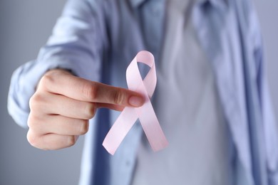 Photo of Woman with pink awareness ribbon on grey background, closeup