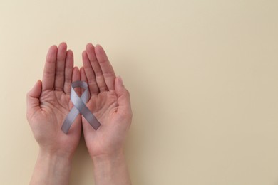 Woman with grey awareness ribbon on beige background, top view. Space for text