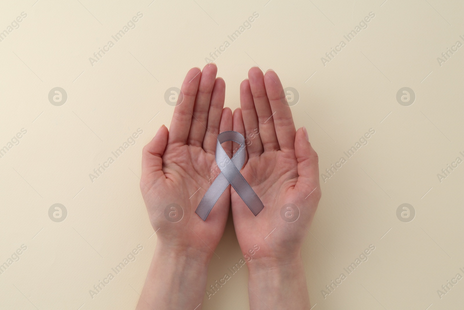 Photo of Woman with grey awareness ribbon on beige background, top view