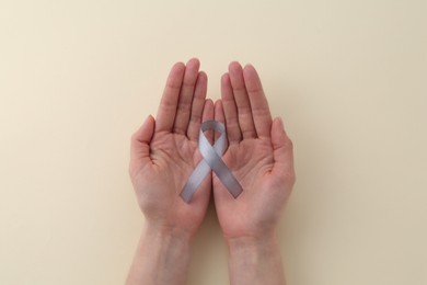 Photo of Woman with grey awareness ribbon on beige background, top view