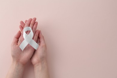 Woman with white awareness ribbon on beige background, top view. Space for text