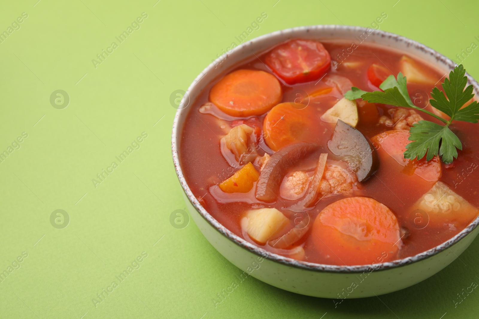 Photo of Delicious homemade stew in bowl on green background, closeup