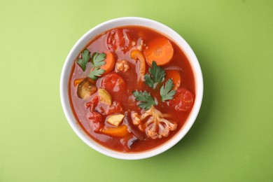 Delicious homemade stew in bowl on green background, top view