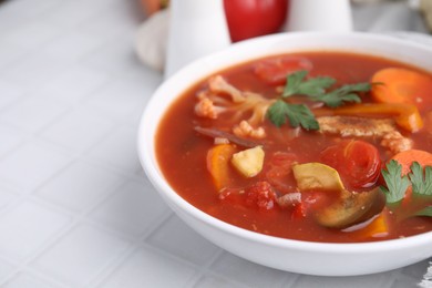 Delicious homemade stew in bowl on white tiled table, closeup