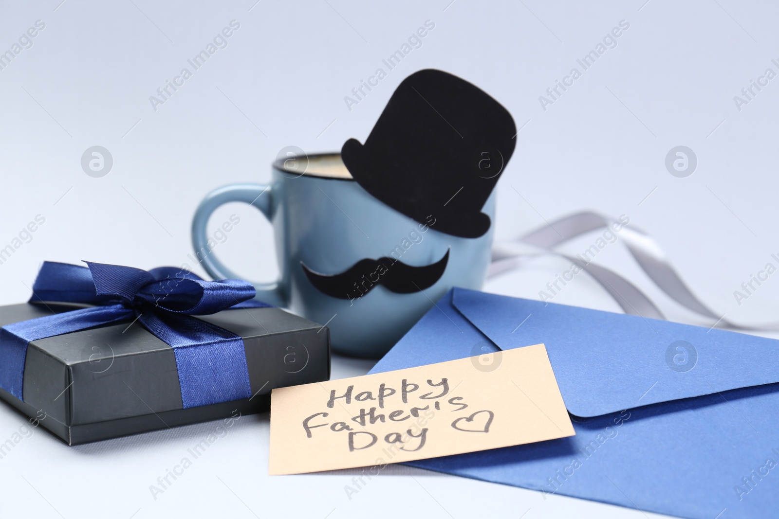 Photo of Greeting card with phrase Happy Father's Day, envelope, gift and cup of coffee on light background