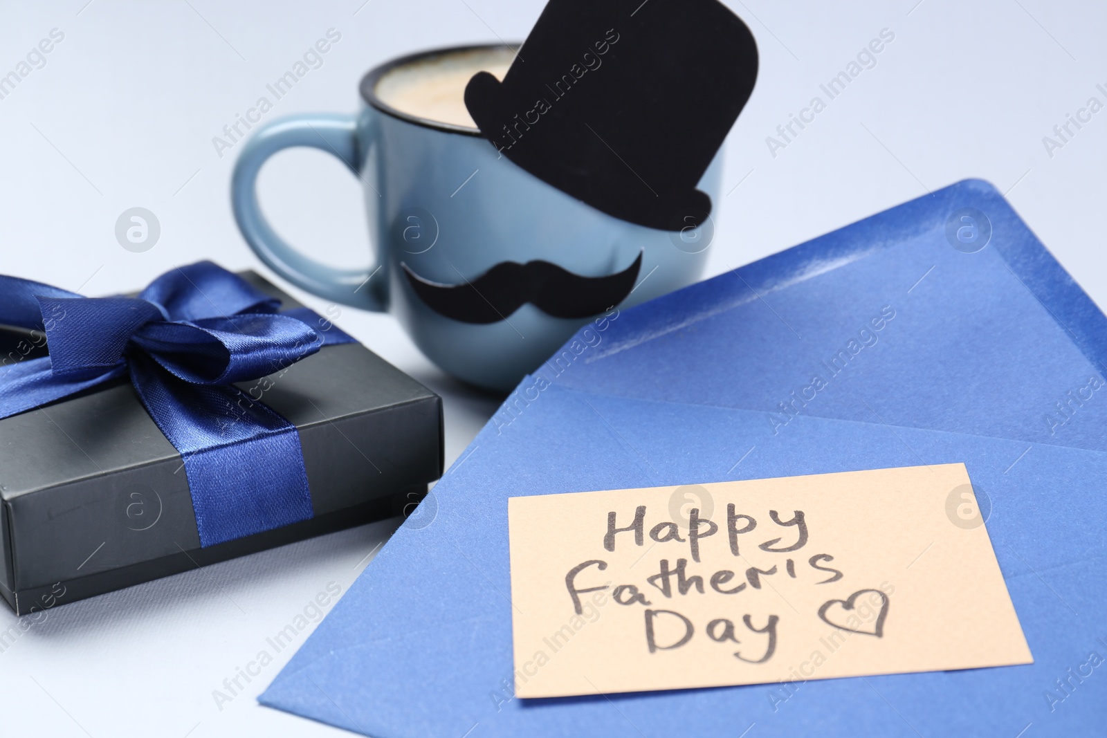 Photo of Greeting card with phrase Happy Father's Day, envelope, gift and cup of coffee on light background