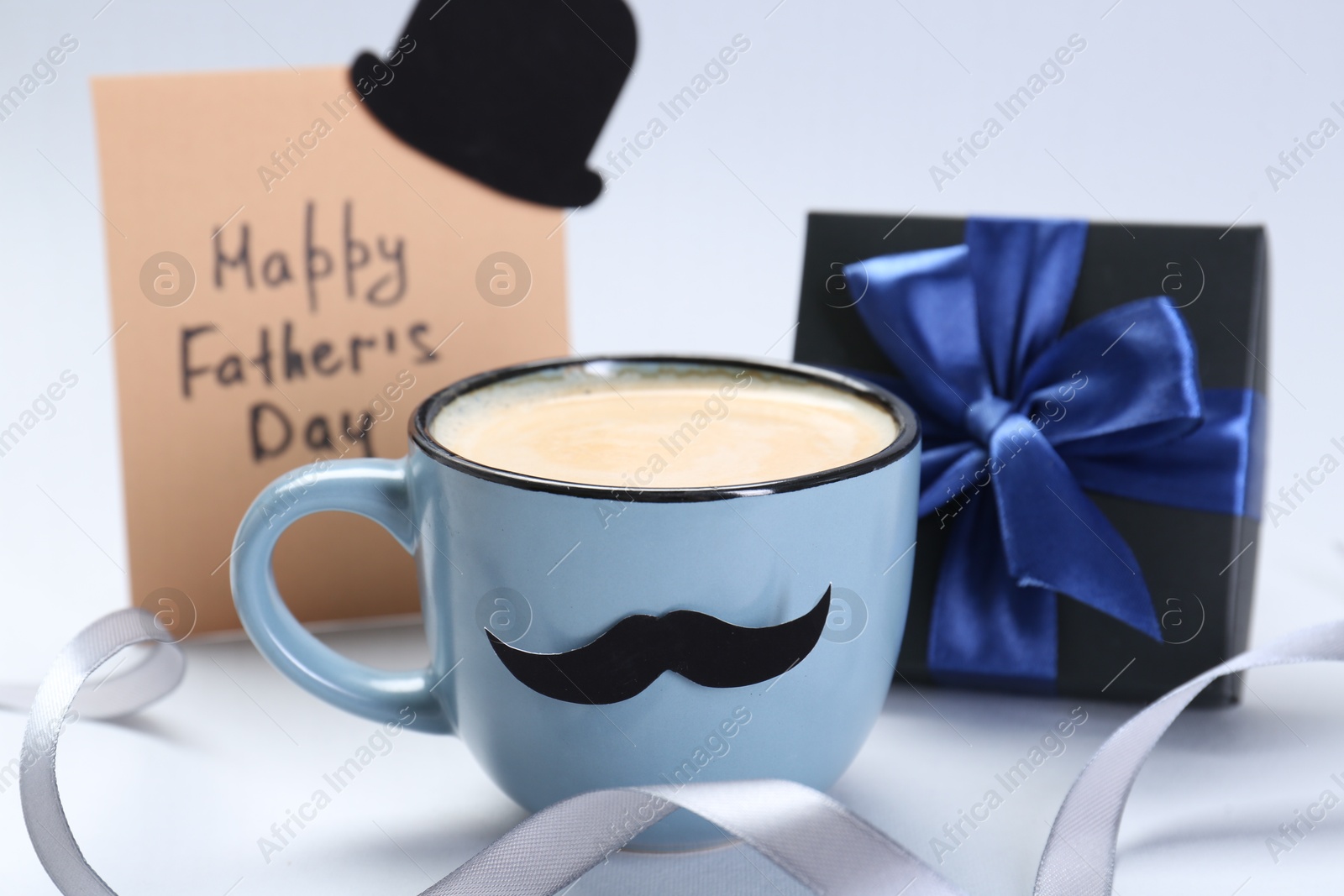 Photo of Greeting card with phrase Happy Father's Day, gift and cup of coffee on light background