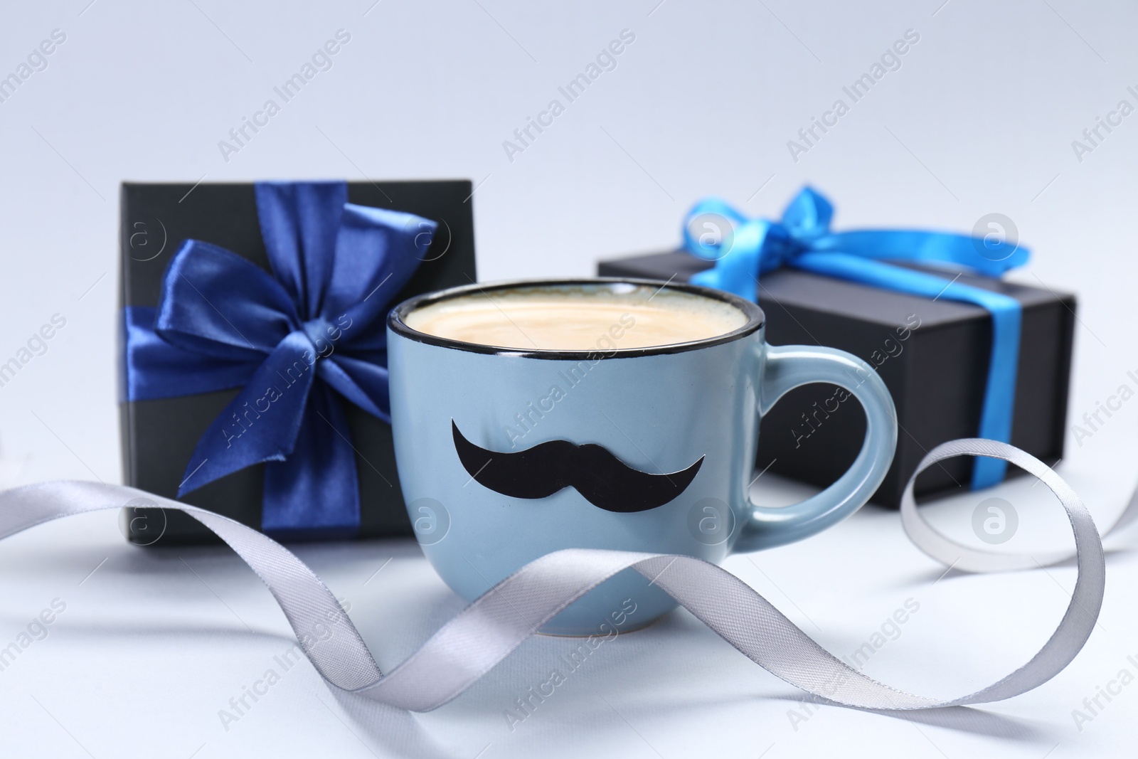 Photo of Happy Father's Day. Cup of coffee with funny moustache and gift boxes on light background