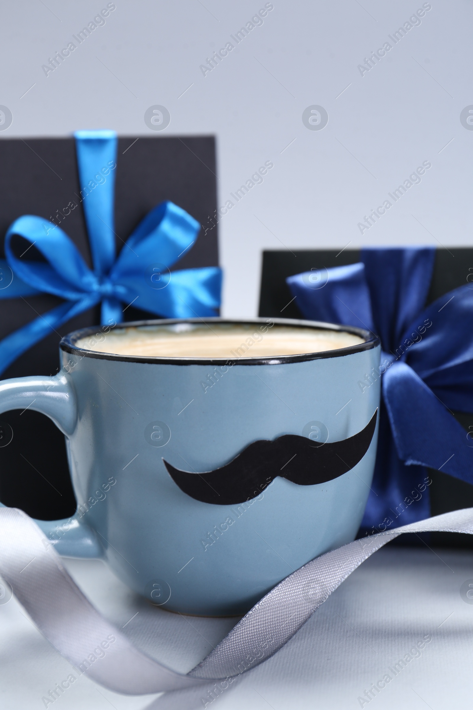 Photo of Happy Father's Day. Cup of coffee with funny moustache and gift boxes on light background