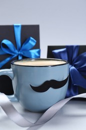 Photo of Happy Father's Day. Cup of coffee with funny moustache and gift boxes on light background