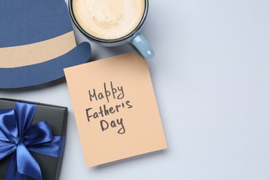 Photo of Greeting card with phrase Happy Father's Day, coffee, gift and paper hat on light background, flat lay. Space for text