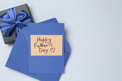 Photo of Greeting card with phrase Happy Father's Day, envelope and gift on light background, top view. Space for text