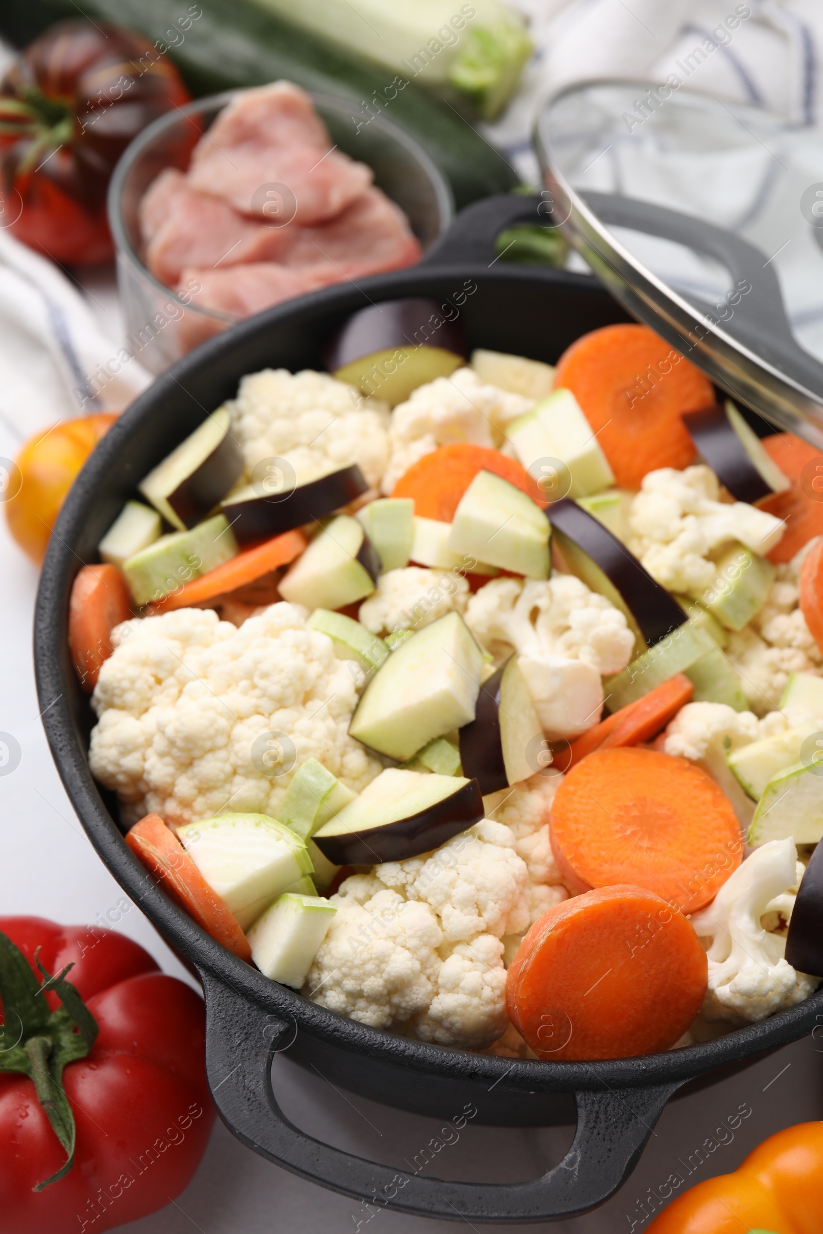 Photo of Cooking stew. Cut raw vegetables in pot and other ingredients on white table, closeup