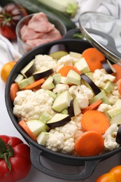 Cooking stew. Cut raw vegetables in pot and other ingredients on white table, closeup