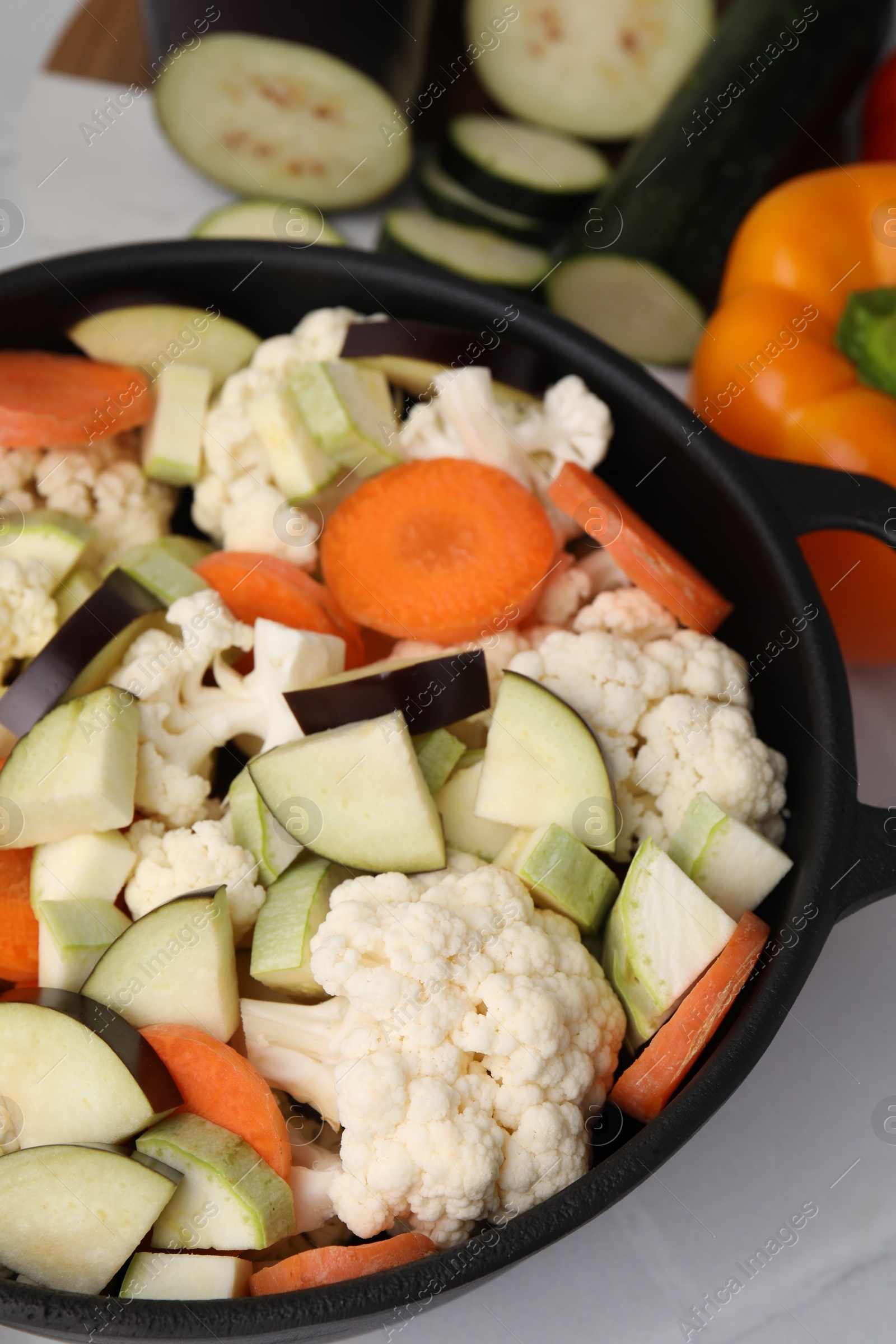 Photo of Cooking stew. Cut raw vegetables in pot on white table, closeup