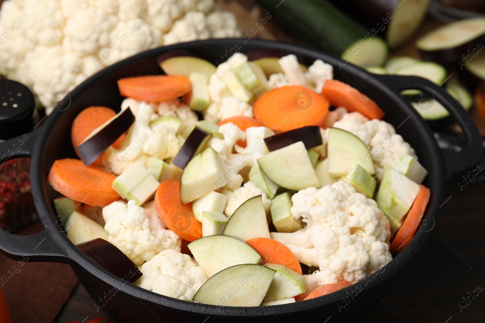 Photo of Cooking stew. Cut raw vegetables in pot on wooden table, closeup