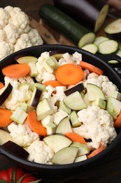 Photo of Cooking stew. Cut raw vegetables in pot on wooden table, closeup