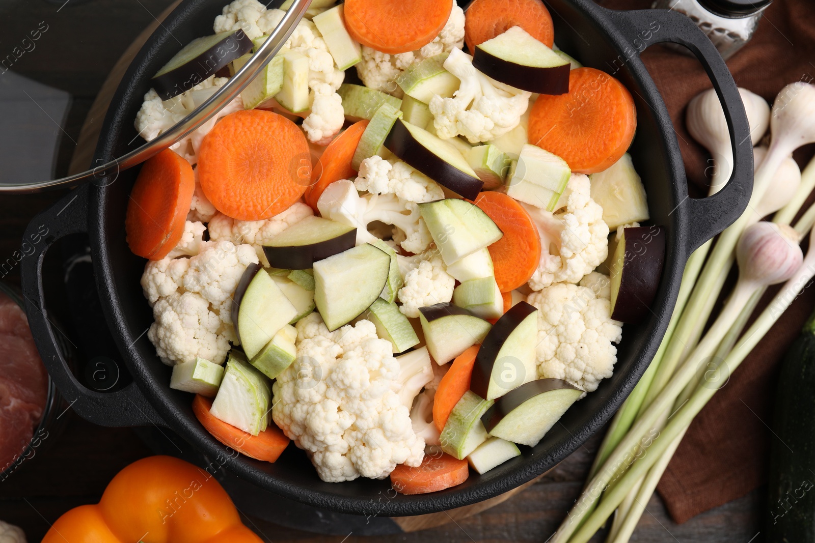 Photo of Cooking stew. Cut raw vegetables in pot on wooden table, flat lay