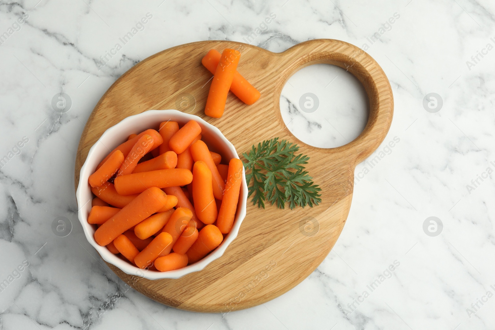 Photo of Baby carrots in bowl and green leaf on white marble table, top view