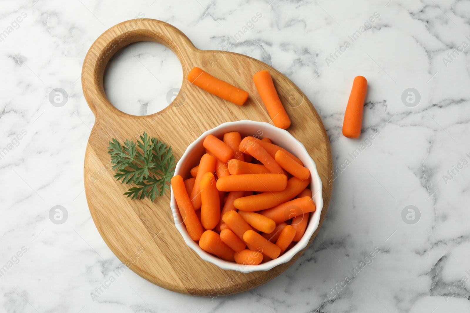 Photo of Baby carrots in bowl and green leaf on white marble table, top view